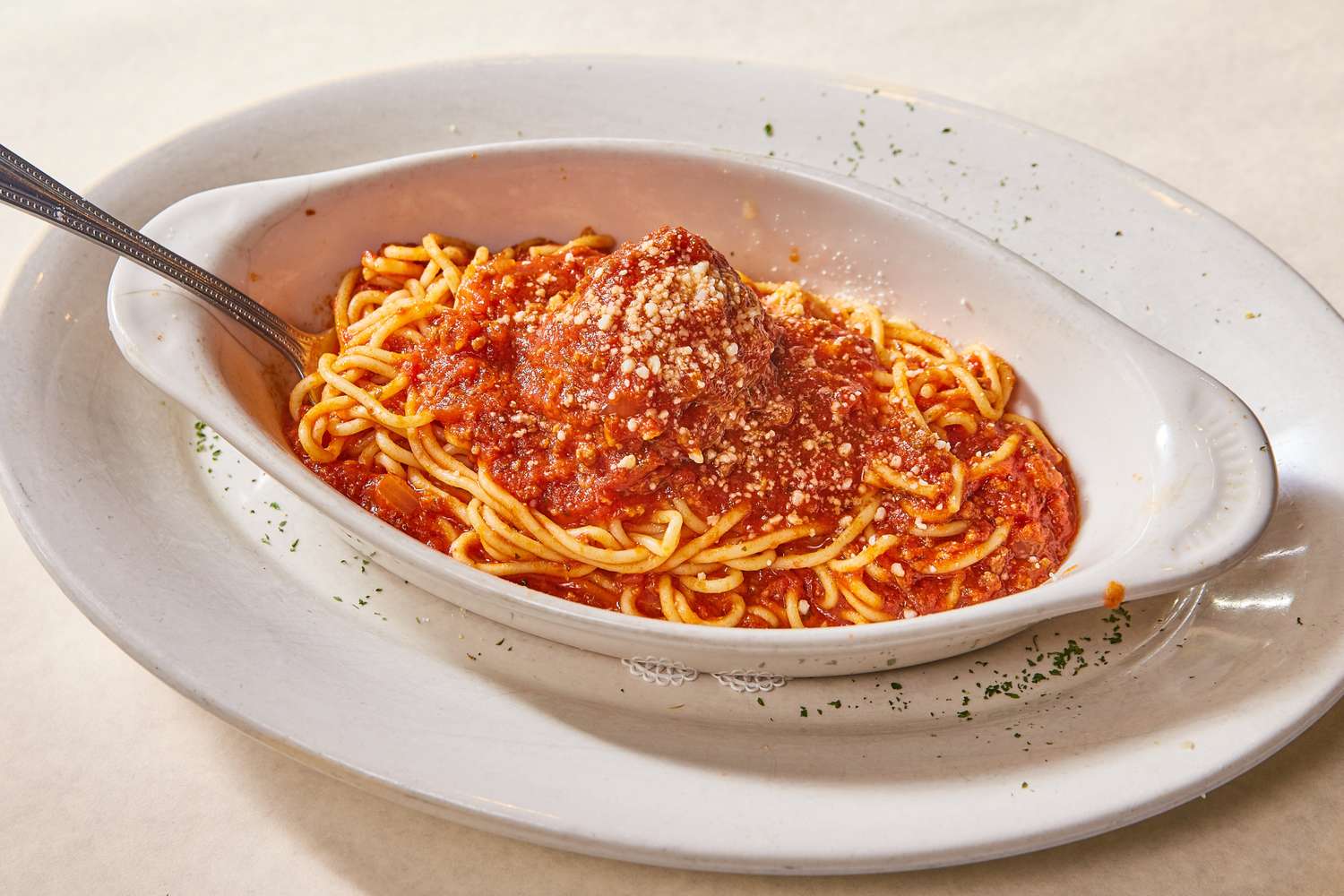 A dish of spaghetti with tomato sauce and parmesan cheese served on a white plate