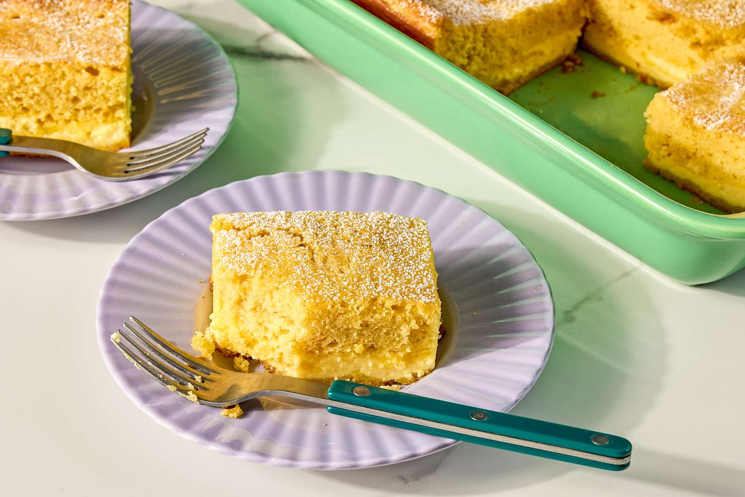 Slices of cake on plates with forks next to a baking dish containing more cake