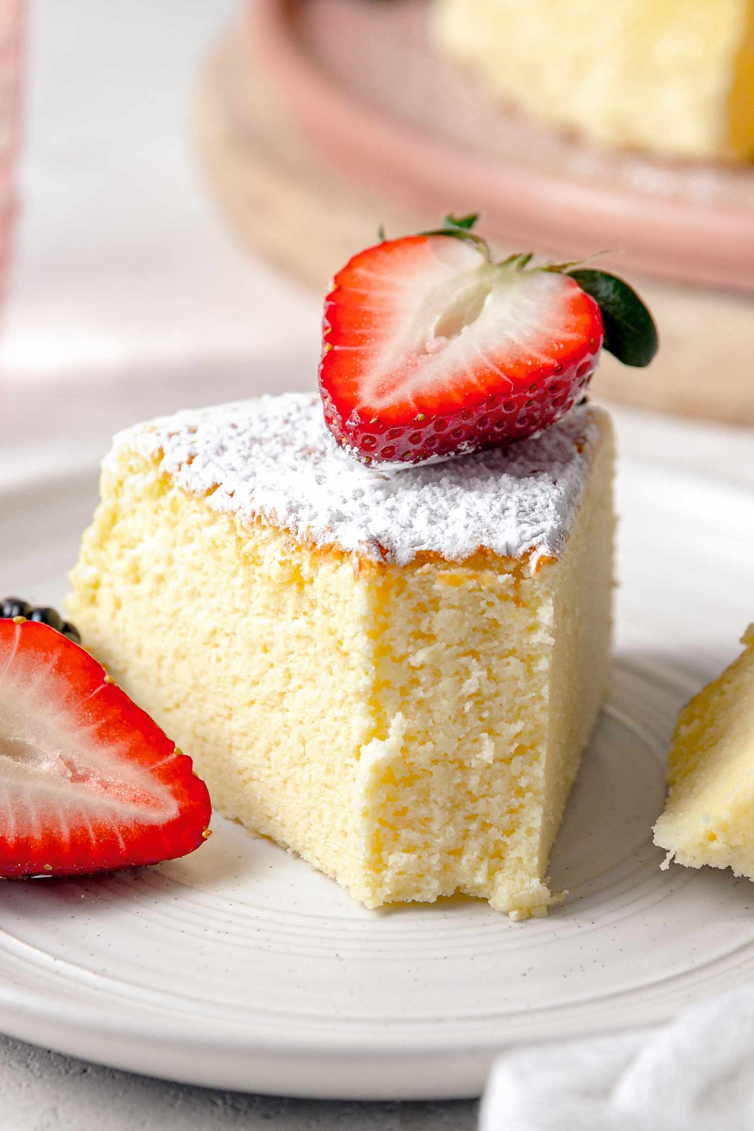 On a Small Plate, a Slice of Japanese Cheesecake With a Bite Size on the Fork Next to It, Served With Halved Strawberries