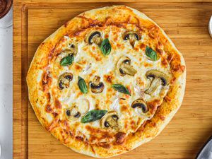 Overhead view of a pizza dough recipe and topped with cheese and mushrooms.