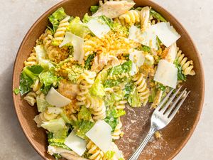A bowl of pasta salad with chicken and shredded cheese on top, fork on the side