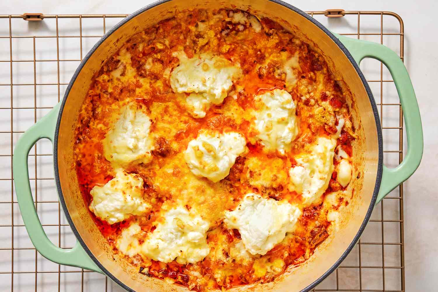 Braised cabbage lasagna in a green pot topped with dollops of ricotta cheese cooling on a wire rack