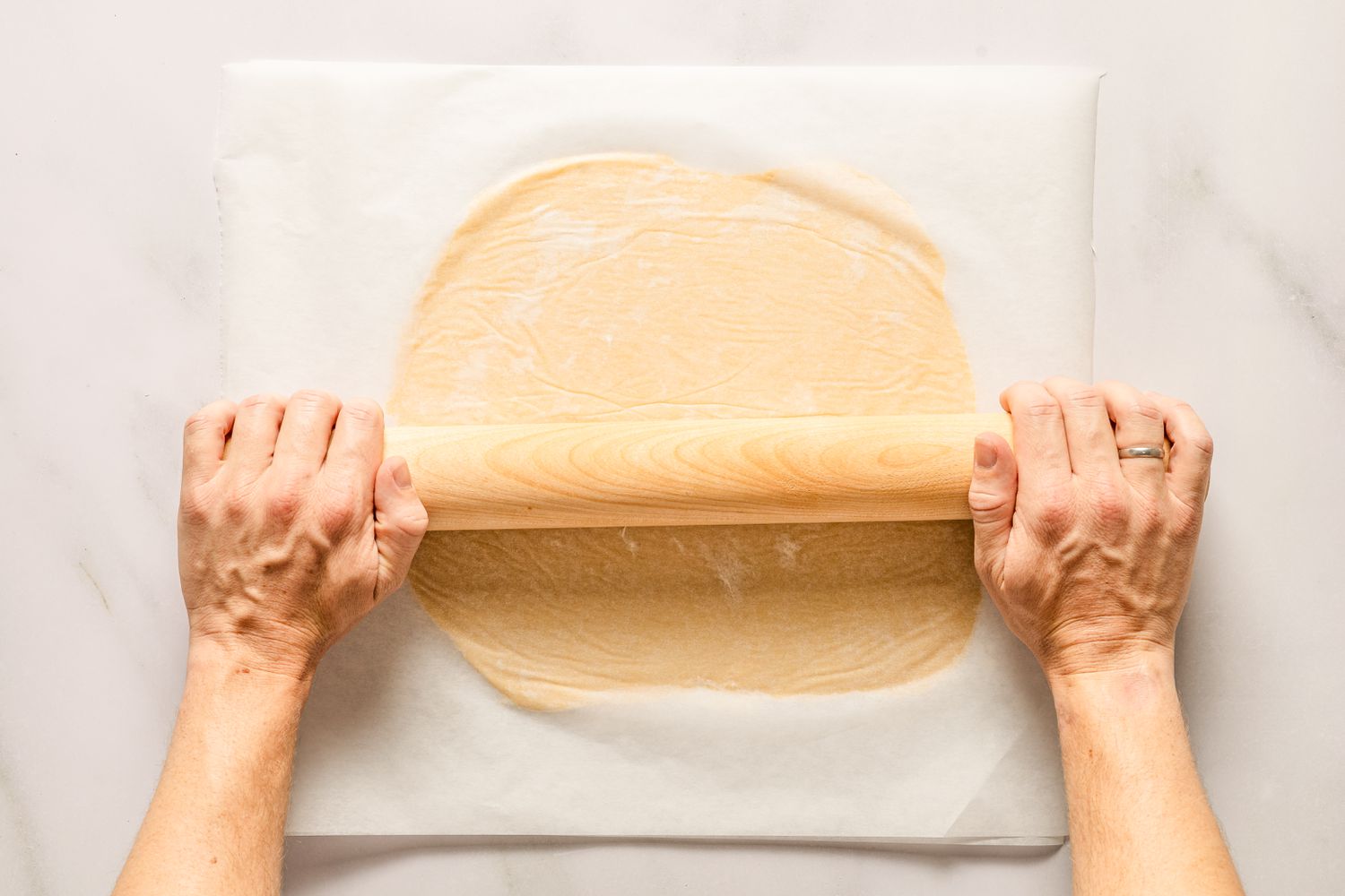 Overhead view of two hands rolling out the dough between sheets of parchment paper for Sand Tarts recipe