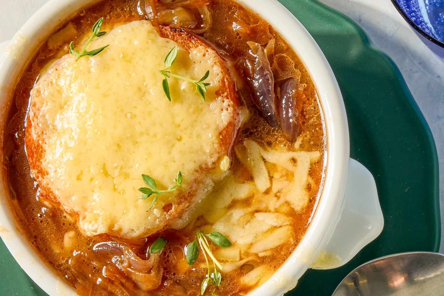 Bowl of French onion soup with melted cheese and bread garnished with fresh herbs