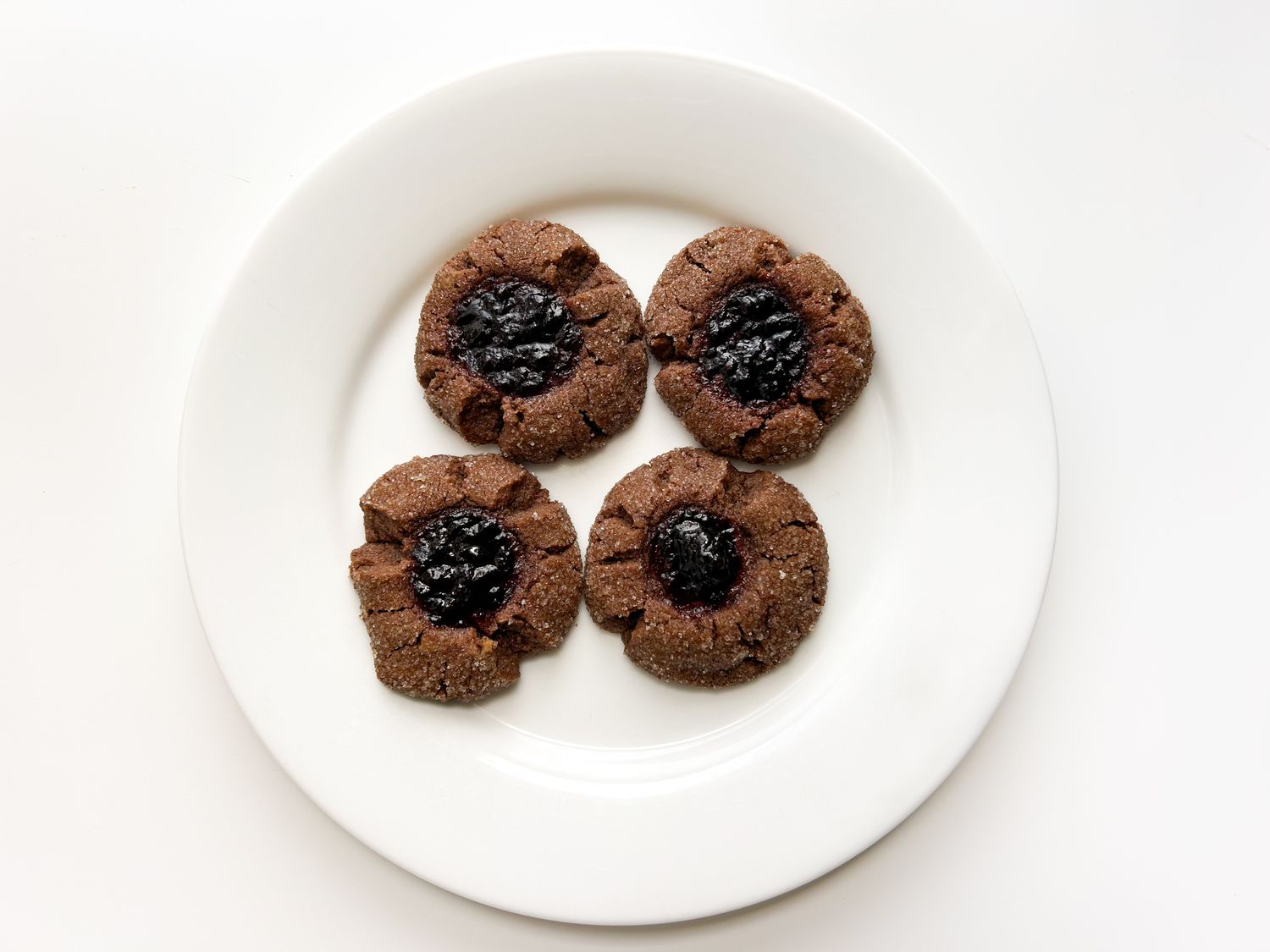 Four cookies with a dark center filling arranged on a white plate