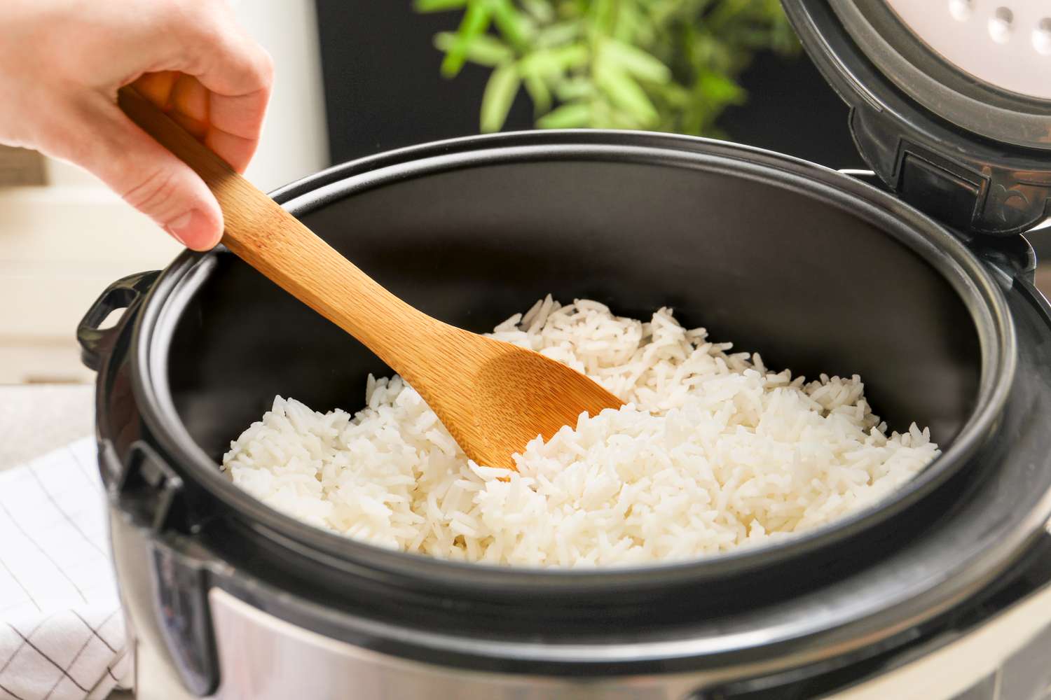 Hand stirring cooked rice in a rice cooker with a wooden spatula