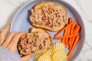 Openface tuna salad sandwiches on a plate with carrot sticks and potato chips
