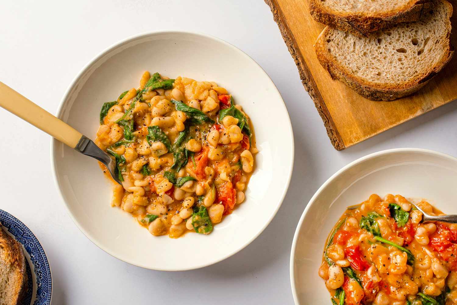 Bowls of stewed beans with tomato and spinach served with bread on the side