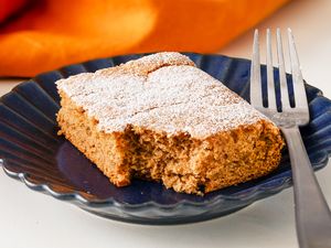 A slice of soda cake topped with powdered sugar on a blue plate accompanied by a fork