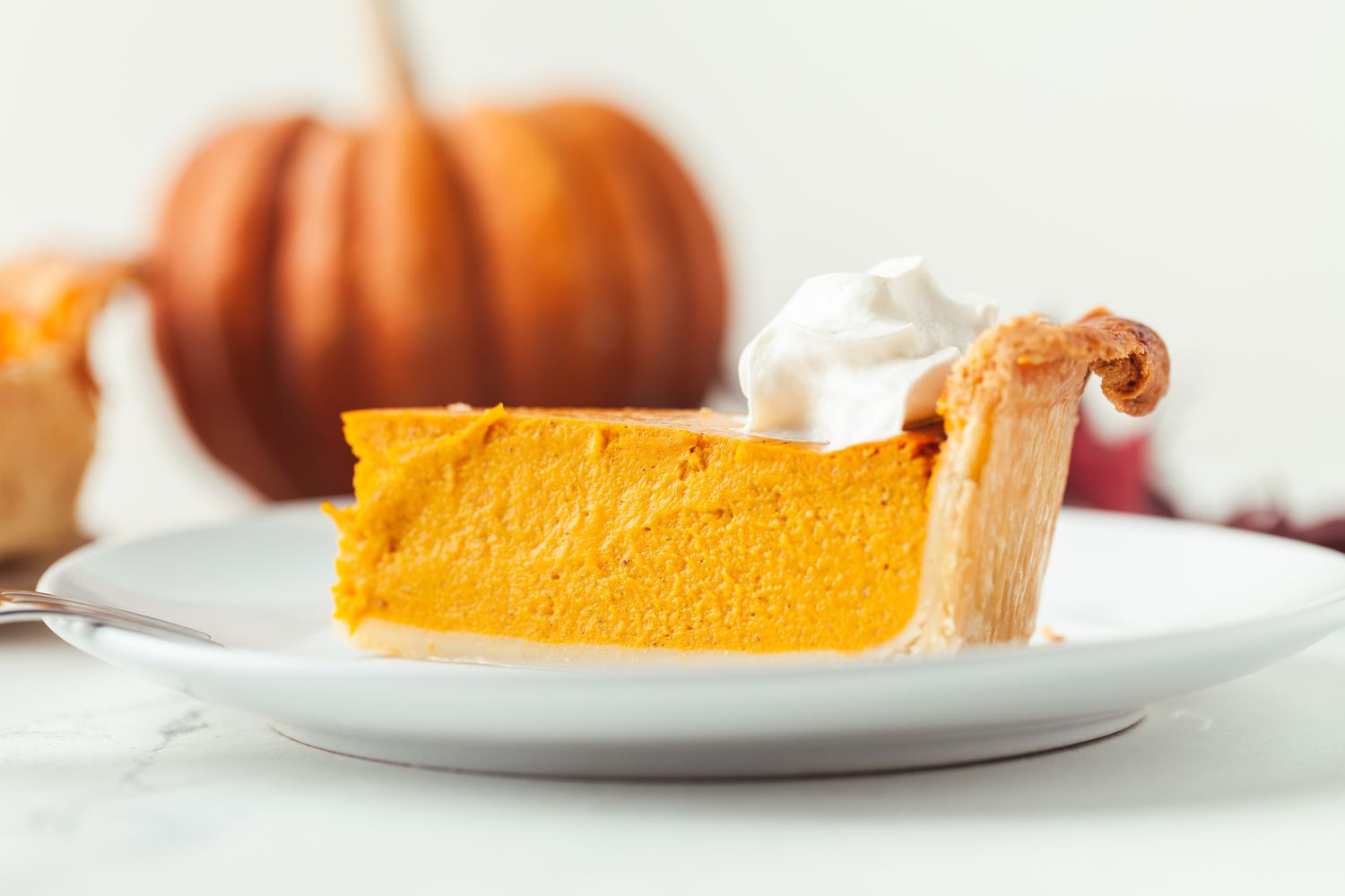 A slice of pumpkin pie on a plate, topped with whipped cream