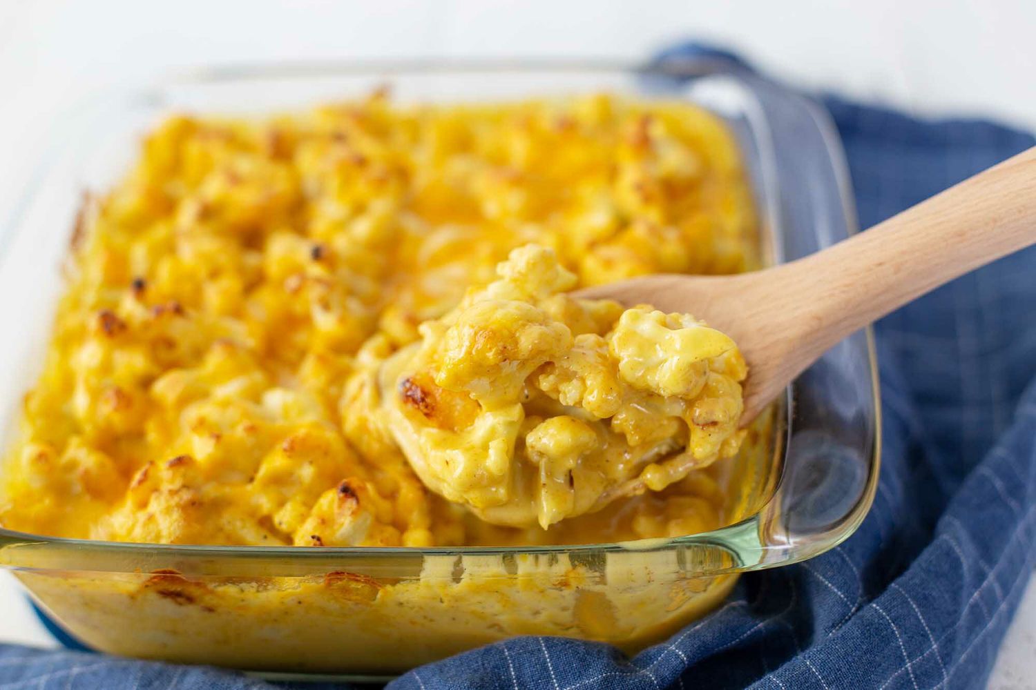 Spoon Scooping a Serving of Cheesy Baked Cauliflower from a Casserole Dish