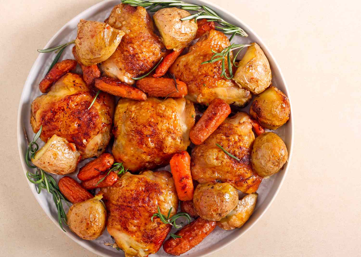 Roasted chicken thighs served with potatoes and carrots on a plate garnished with herbs