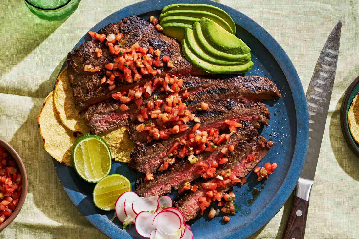 A platter of sliced carne asada topped with salsa and garnished with sliced avocado 