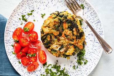 Plate of Bubble and Squeak Topped with Herbs and Side of Halved Cherry Tomatoes with a Fork