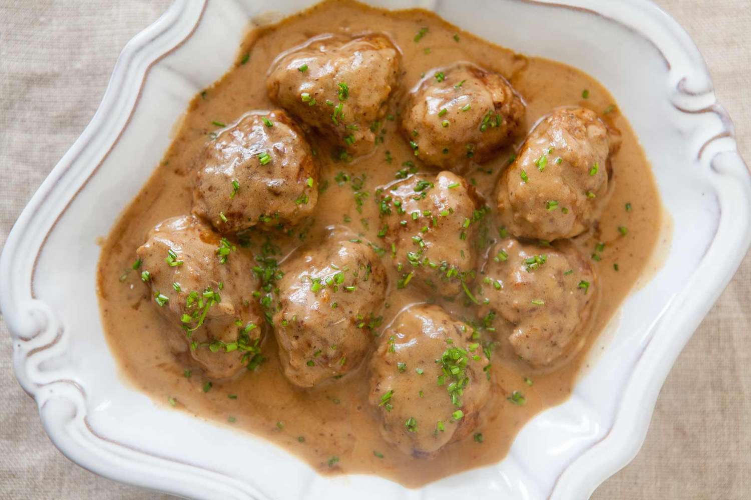 A dish of Swedish meatballs in creamy sauce garnished with herbs