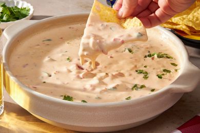 Corn chip with chile con queso cascading off it into a bowl with more chile con queso (at a table setting)
