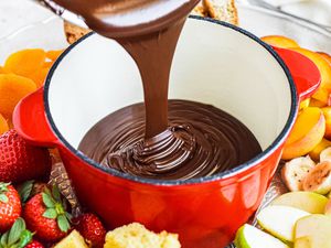 Fondue chocolate poured into a small pot surrounded by cut fruit