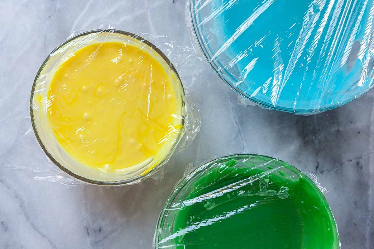 Three glass bowls with colorful royal icing inside.