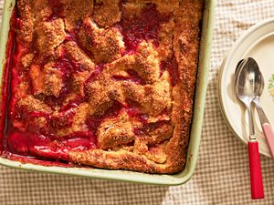peach and raspberry pandowdy in a casserole dish next to a stack of plates on comfy (cottage-core style) table 