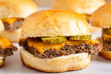 A tray of ovenbaked sliders with beef patties cheddar cheese and pickles in soft buns