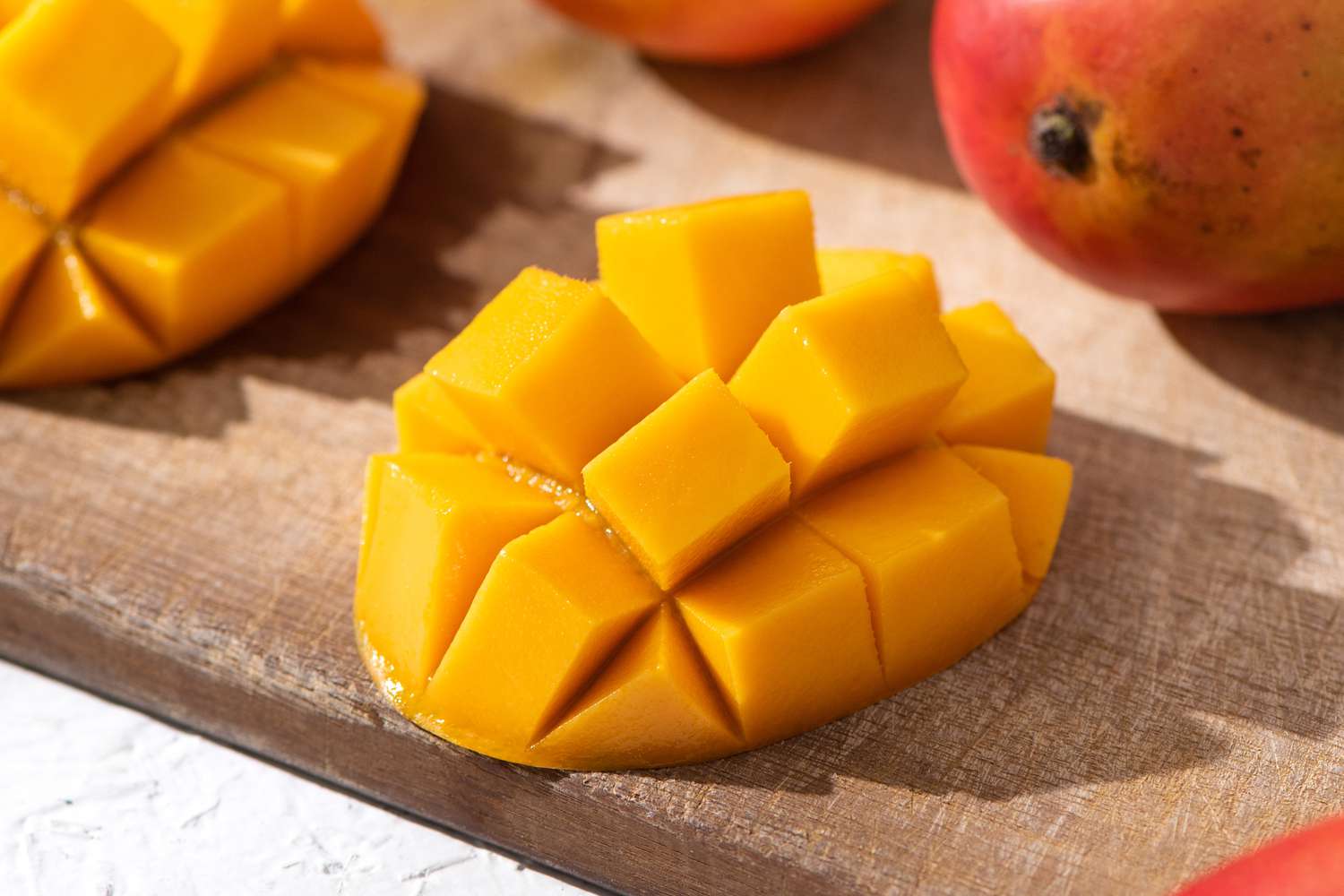 diced mangoes (still attached to skin) on a cutting board next to uncut mangoes