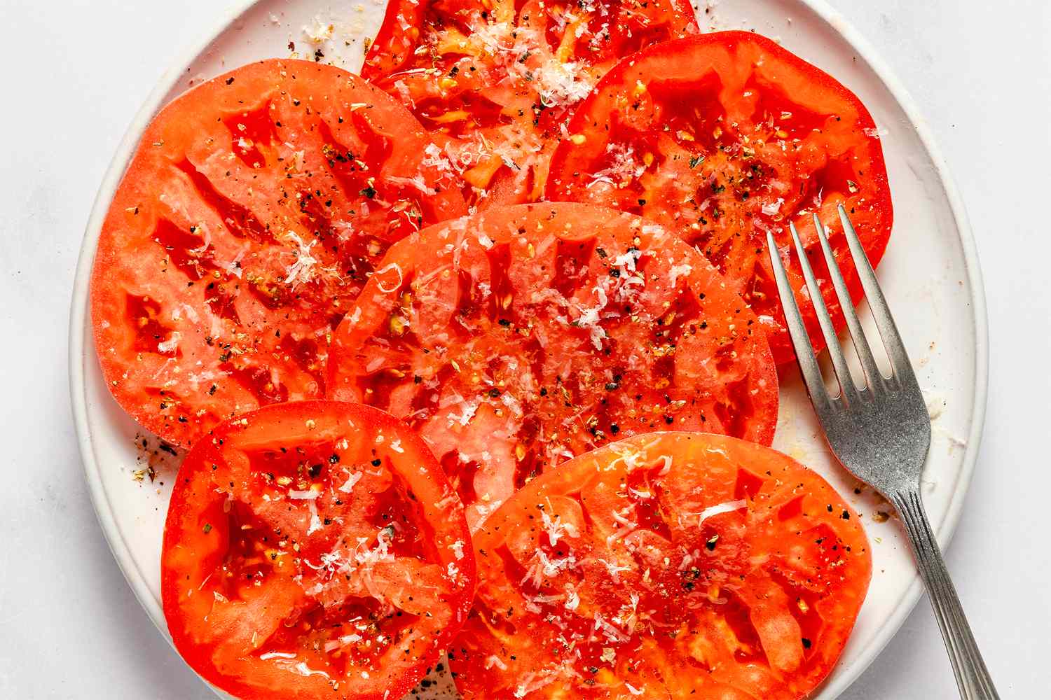 Sliced tomatoes on a plate with seasoning and a fork