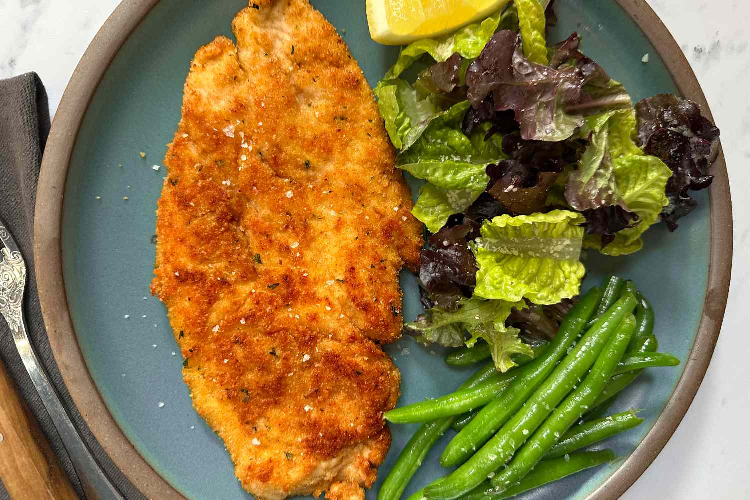 Overhead shot of Ina Garten's parmesan chicken on a plate with green beans and a side salad