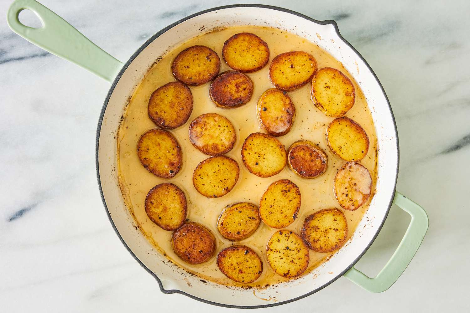 Roasted potato slices in a miso broth in a skillet for the miso melting potatoes recipe