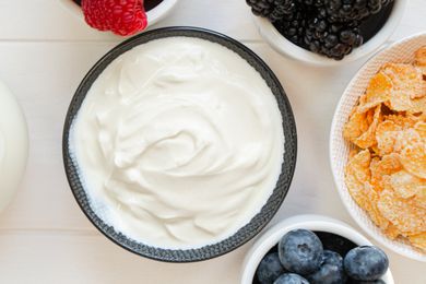 A bowl filled with yogurt next to other bowls with berries and corn flakes