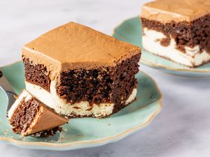 A slice of chocolate cake with a creamy filling on a green plate, a fork with a piece
