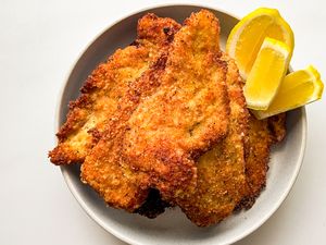 Breaded chicken cutlets served on a plate with lemon wedges