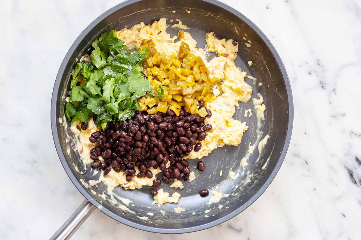 Overhead view of scrambled eggs in a skillet. Black beans, cilantro and green chiles are piled on top of the scrambled eggs.