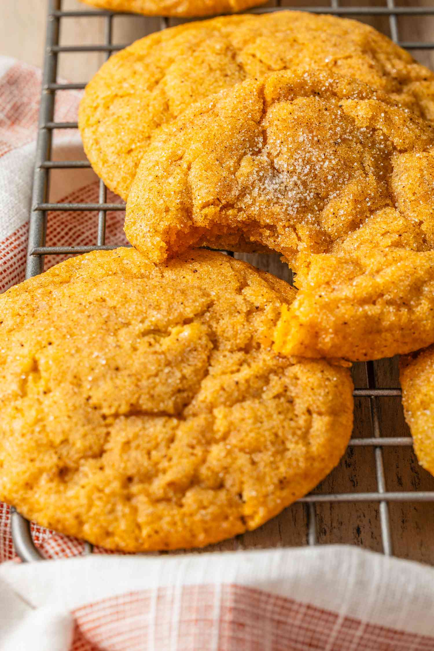 Pumpkin spice snickerdoodle cookies with pumpkin spice sugar mixture (one cookie is missing a bite) on a cooling rack.