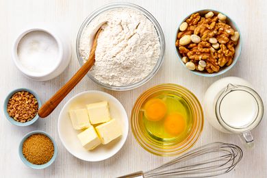 Baking ingredients: flour, eggs, sugar, butter, milk, nuts and spices on a white wooden background