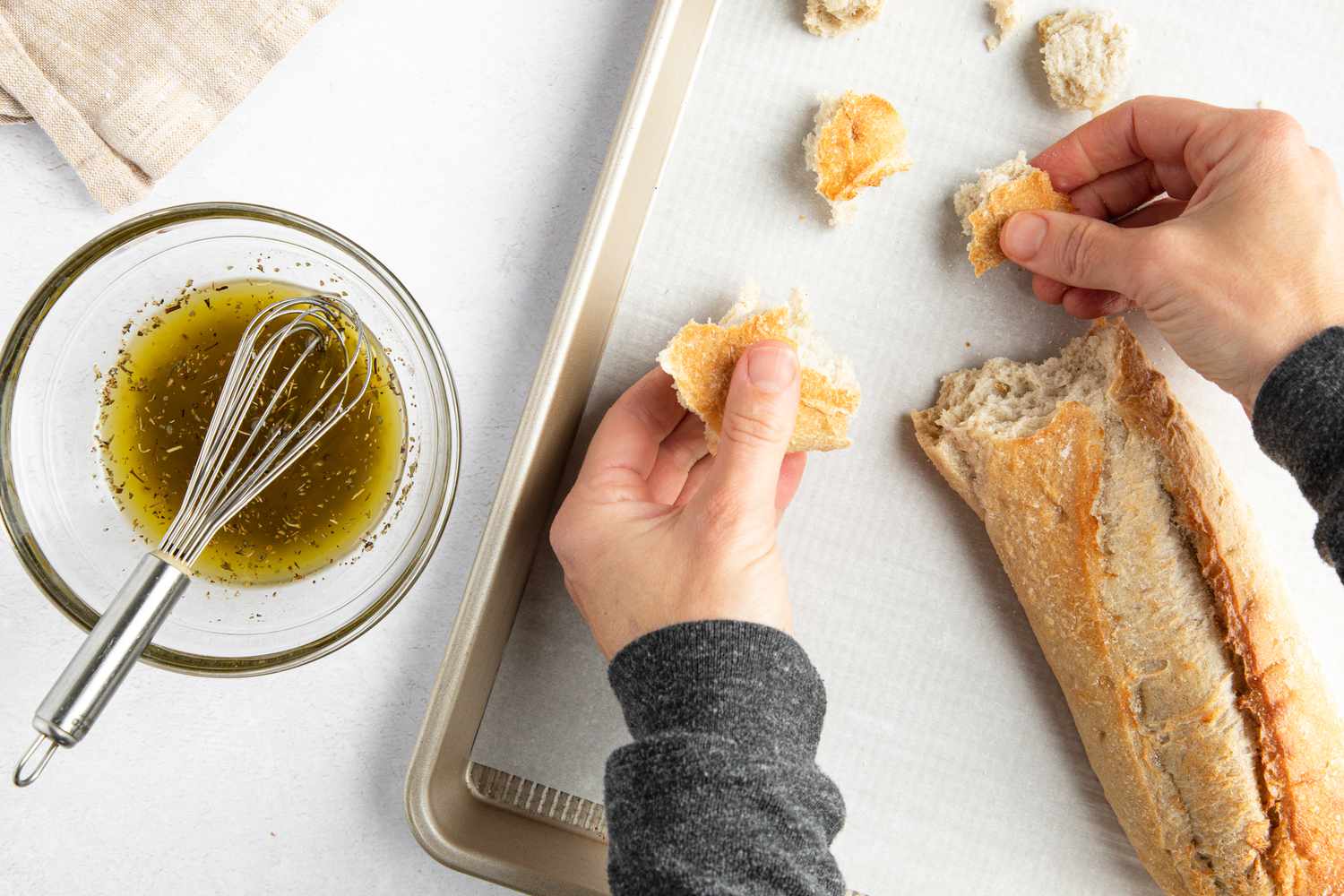 Baguette torn into pieces and onto a baking sheet next the bowl of seasoning for sheet pan caesar salad recipe