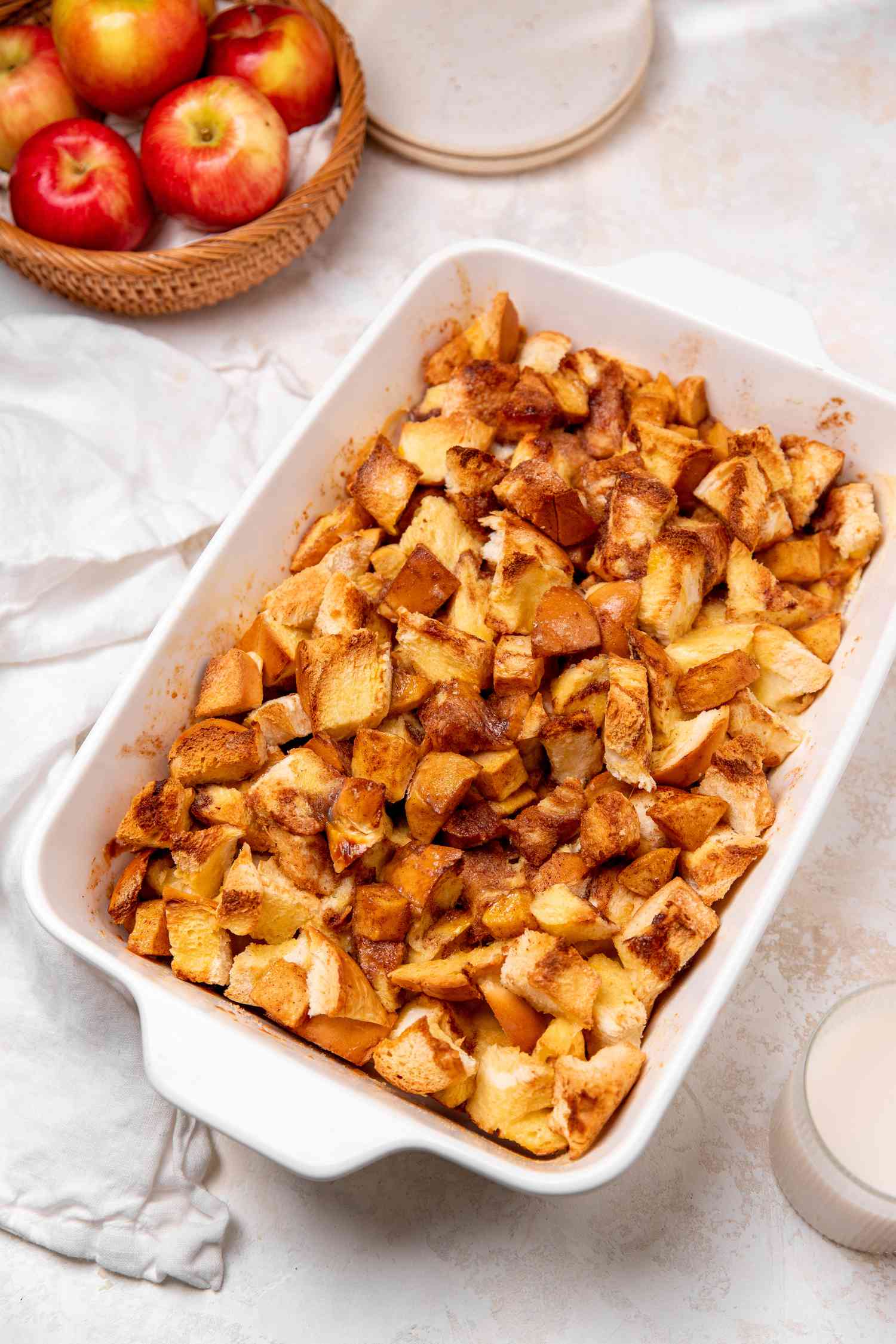 Apple Bread Pudding on a Plate in a Casserole Dish Next to a Bowl of Apples