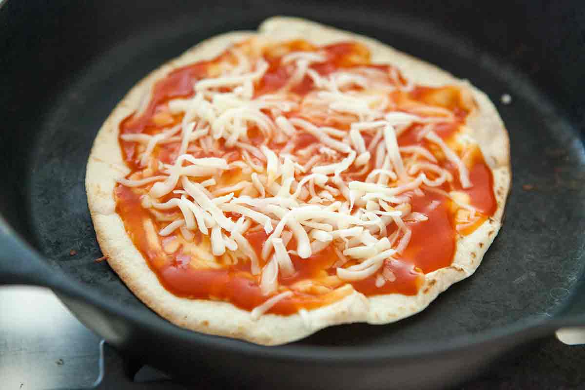 tortilla pizza in cast iron pan with toppings
