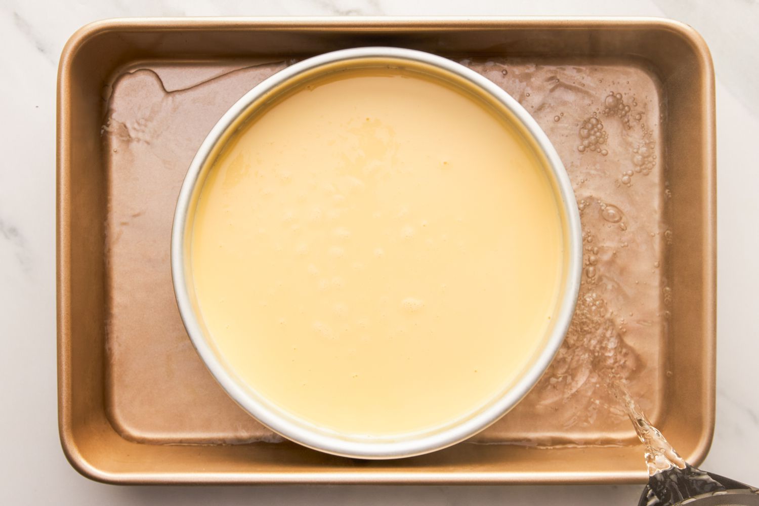Flan ready to bake, sitting in a roasting pan with hot water being added