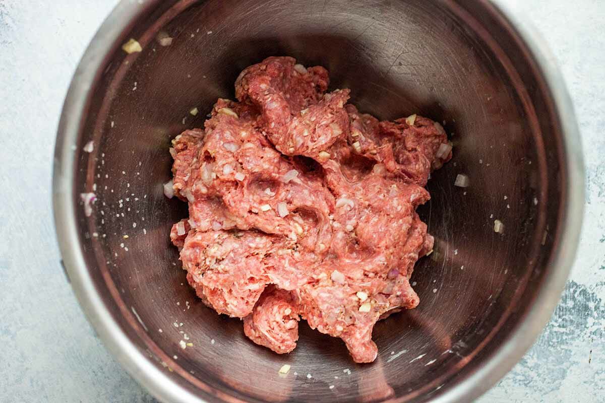 Ground beef and seasonings for grilled burgers mixed together in a bowl