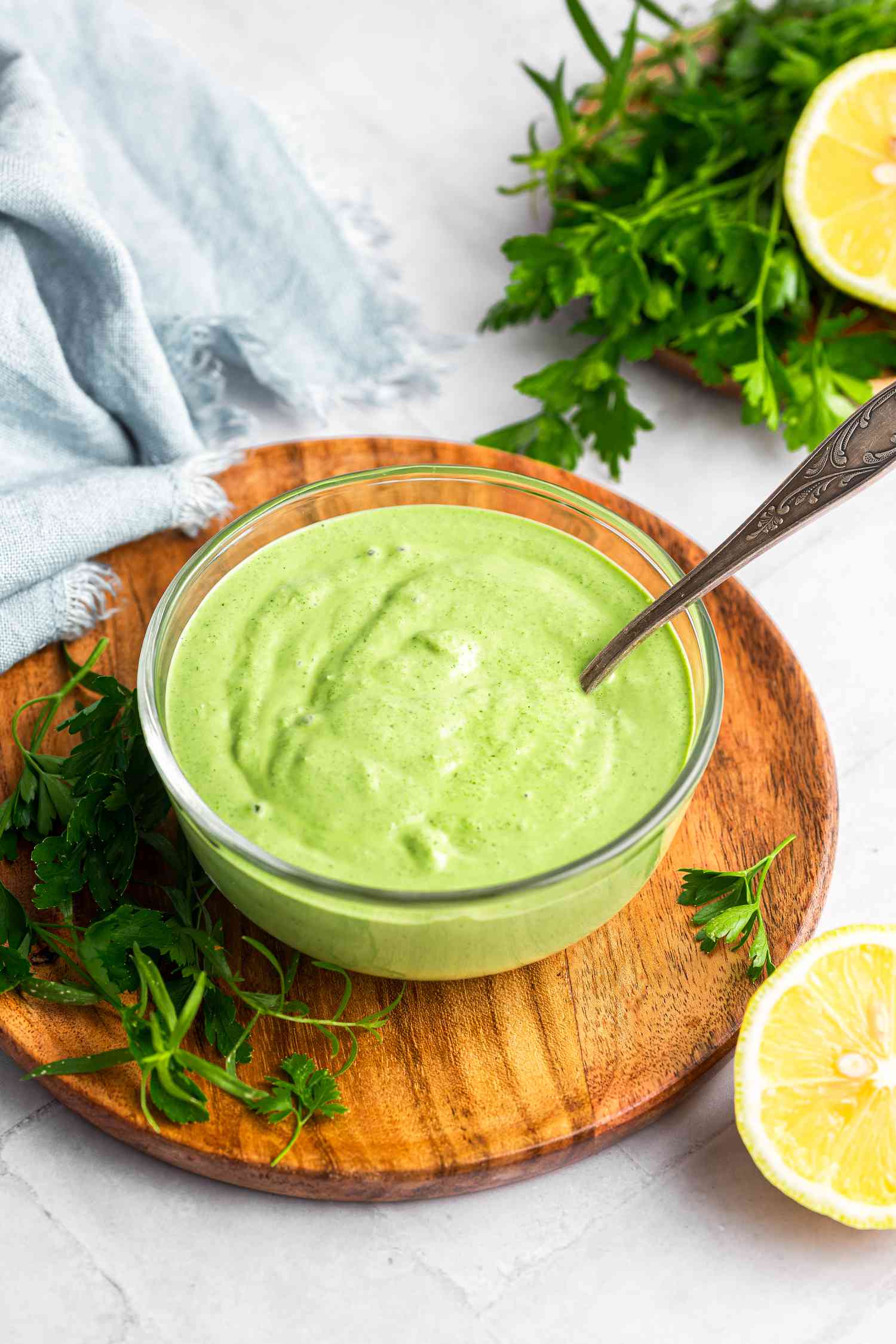 Green Goddess Dressing Recipe in a Bowl Surrounded by Herbs and Halved Lemons