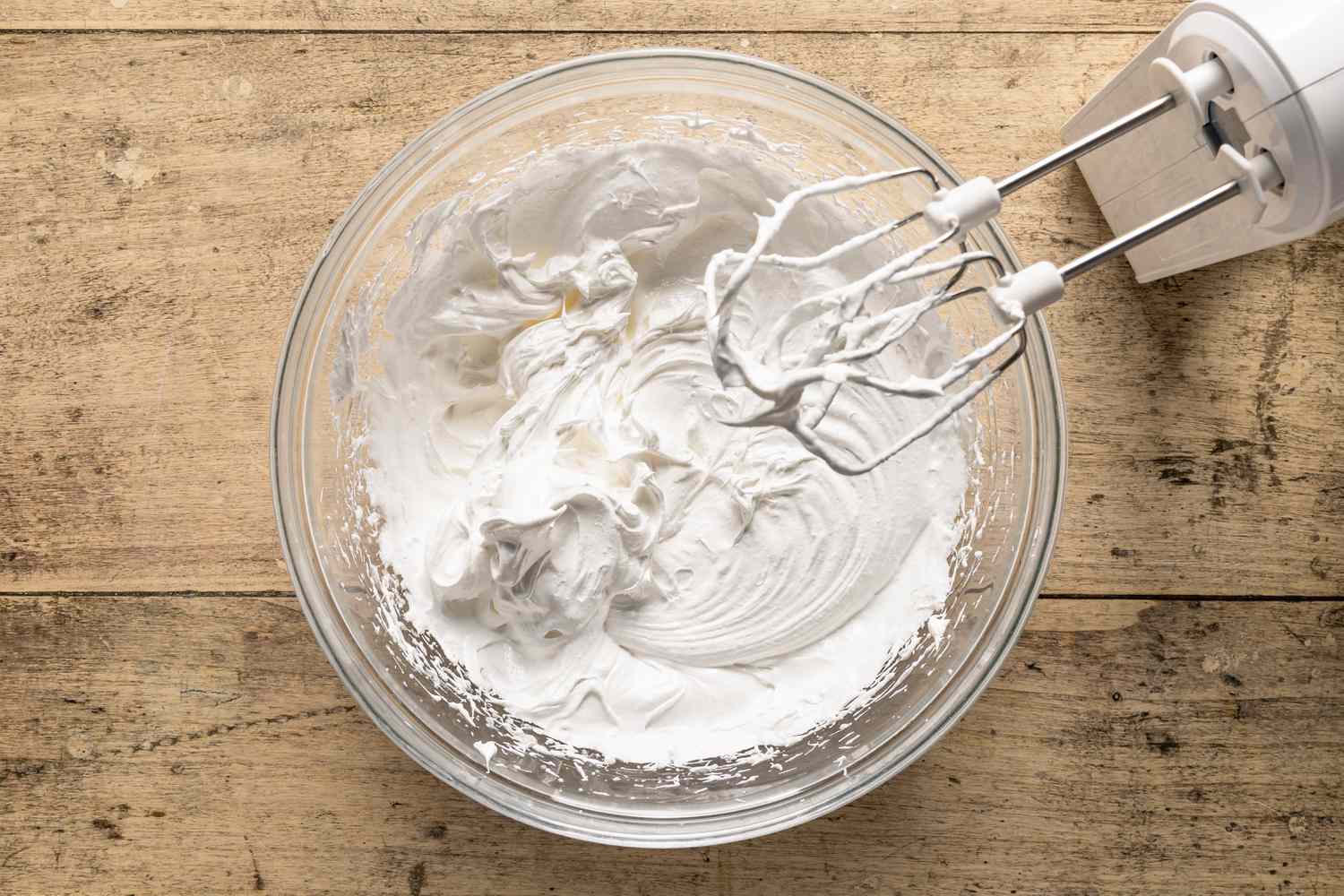 Overhead view of a clear glass bowl with an electric hand mixer after finishing the mixing of egg whites and cream of tartar for Company's Coming Pie recipe