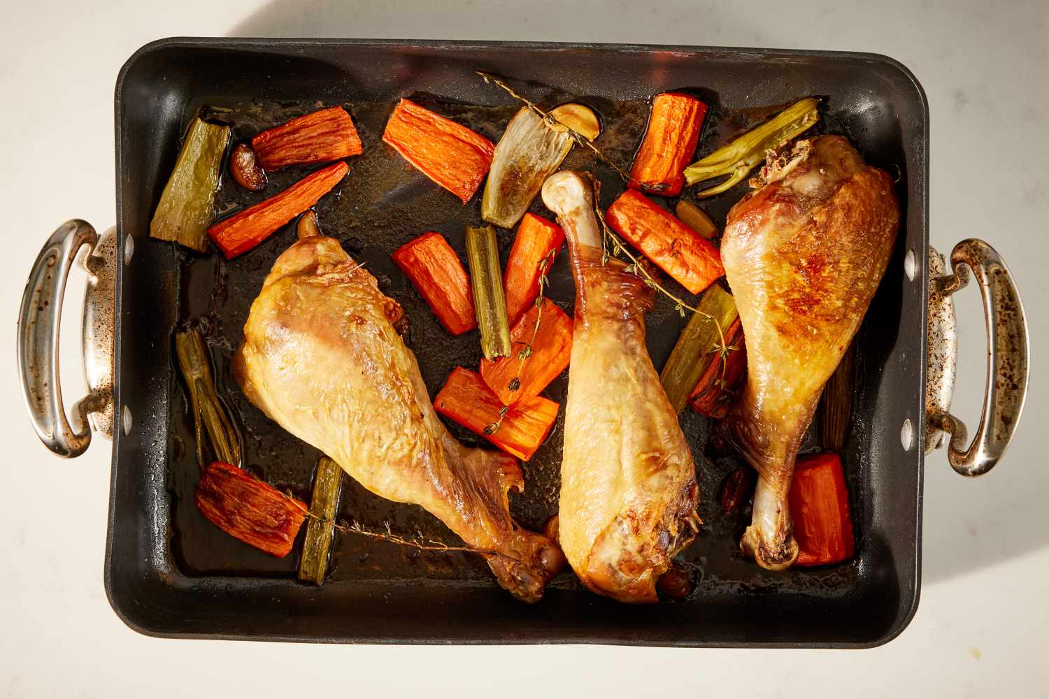 Overhead view of a non-stick baking pan of three turkey legs, carrots, celery and spices on a beige background for Best Ever Gravy recipe