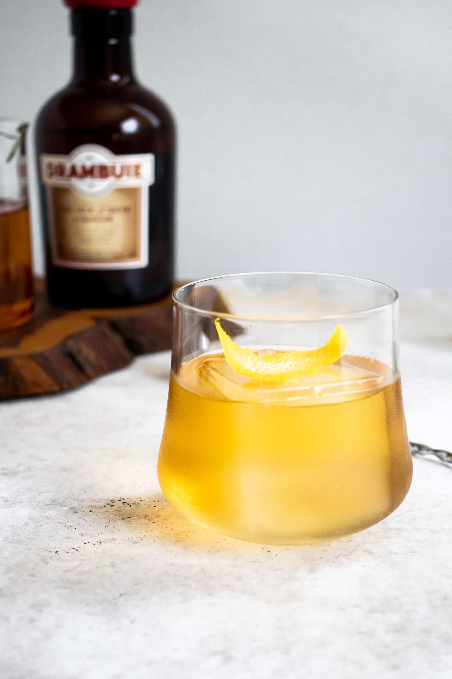 Rusty Nail Garnished with a Lemon Peel with Ingredients in the Background