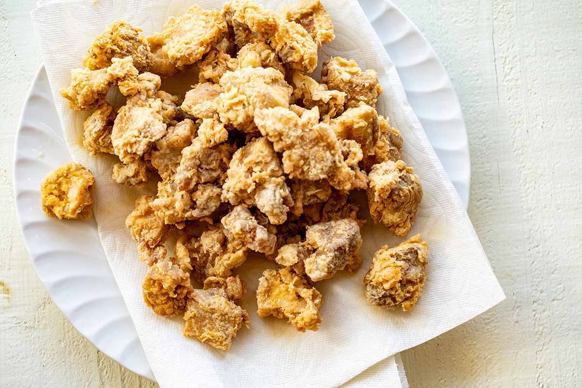 Fried chopped chicken pieces on a scalloped white plate with a white paper towel underneath the chicken.