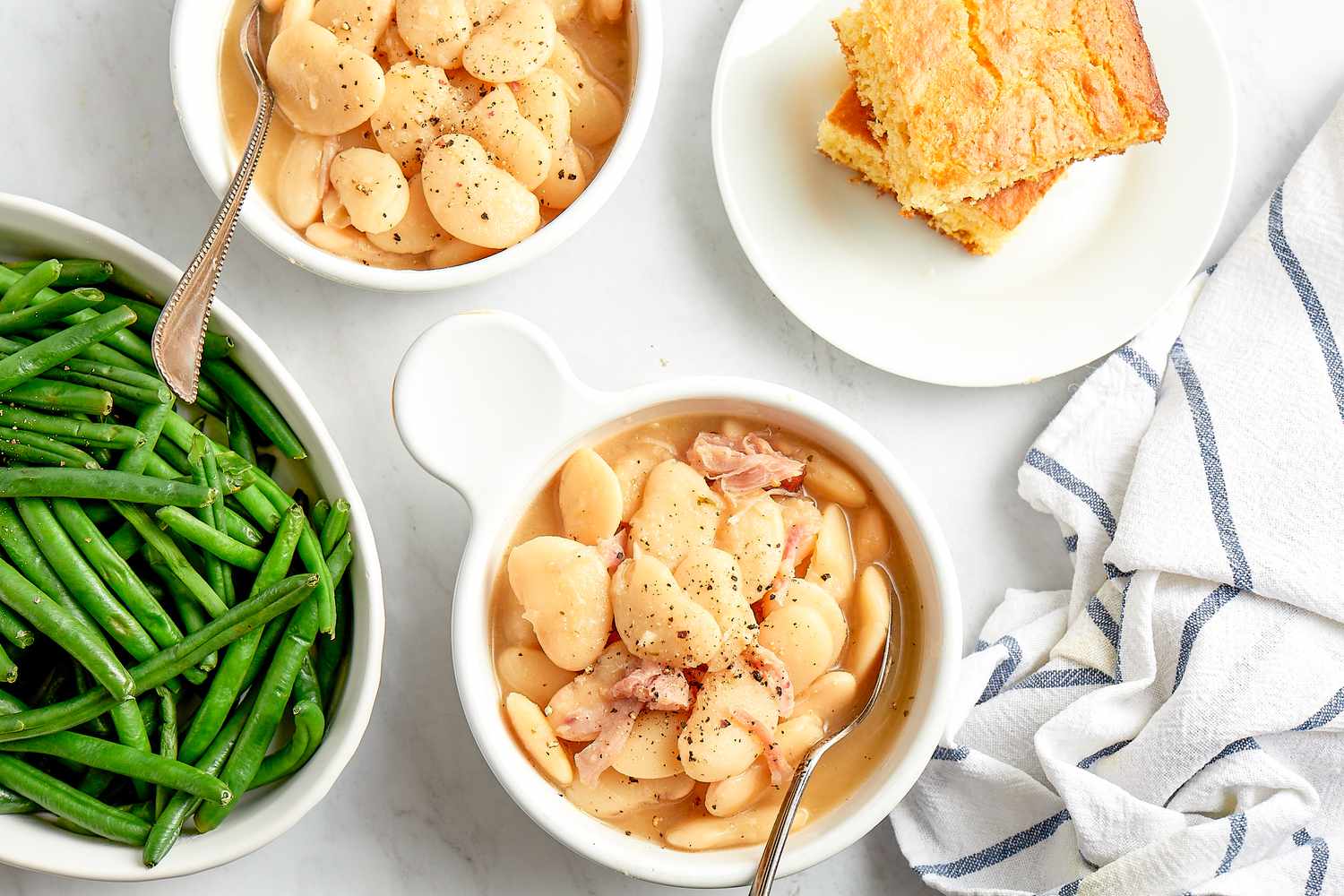 Creamy Southern Lima Beans in Two Bowls Next to Bowl with Green Beans and a Plate with Cornbread 