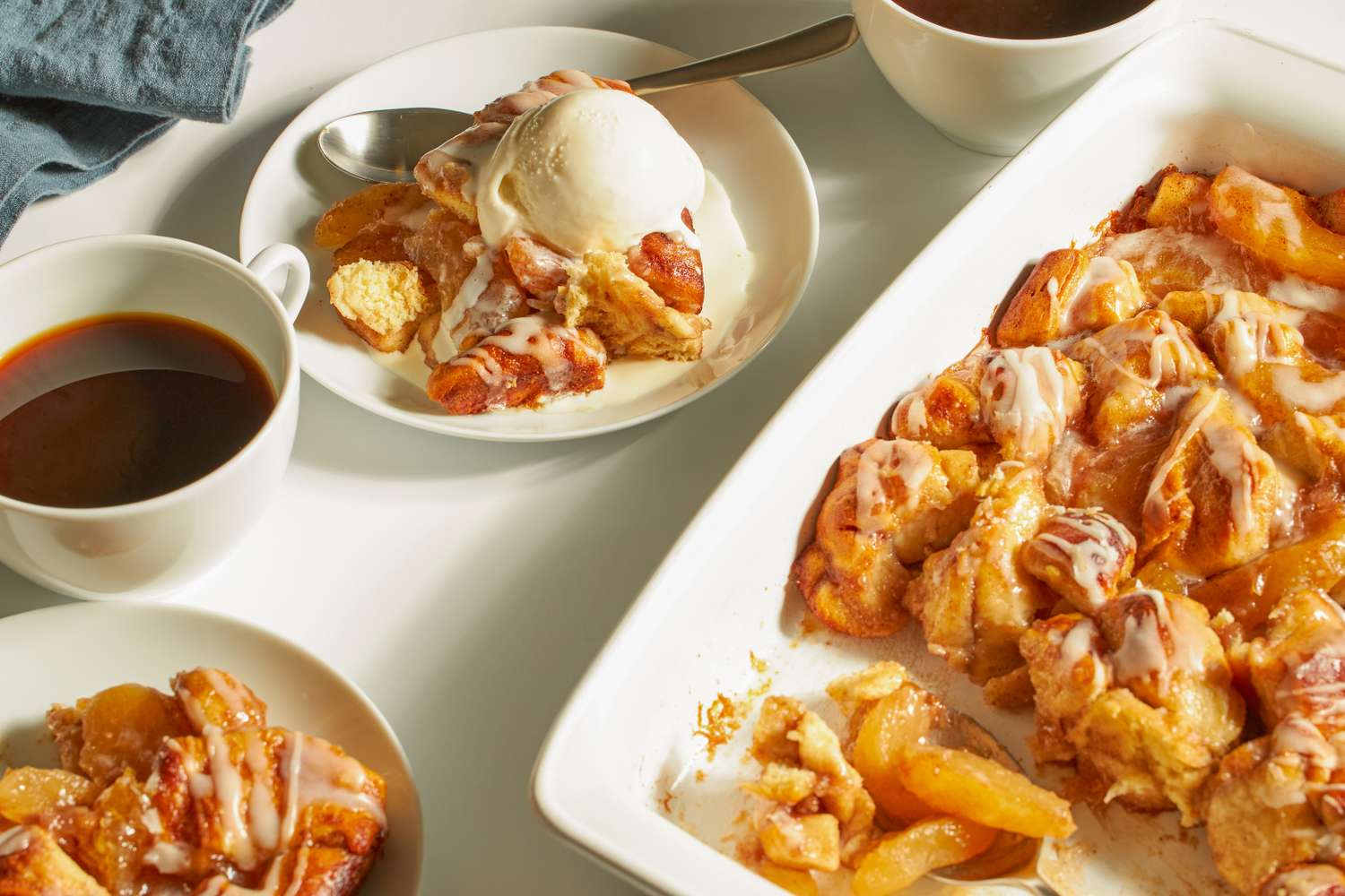 Apple cinnamon cobbler in a baking dish with a plated serving topped with ice cream and cups of coffee on the side