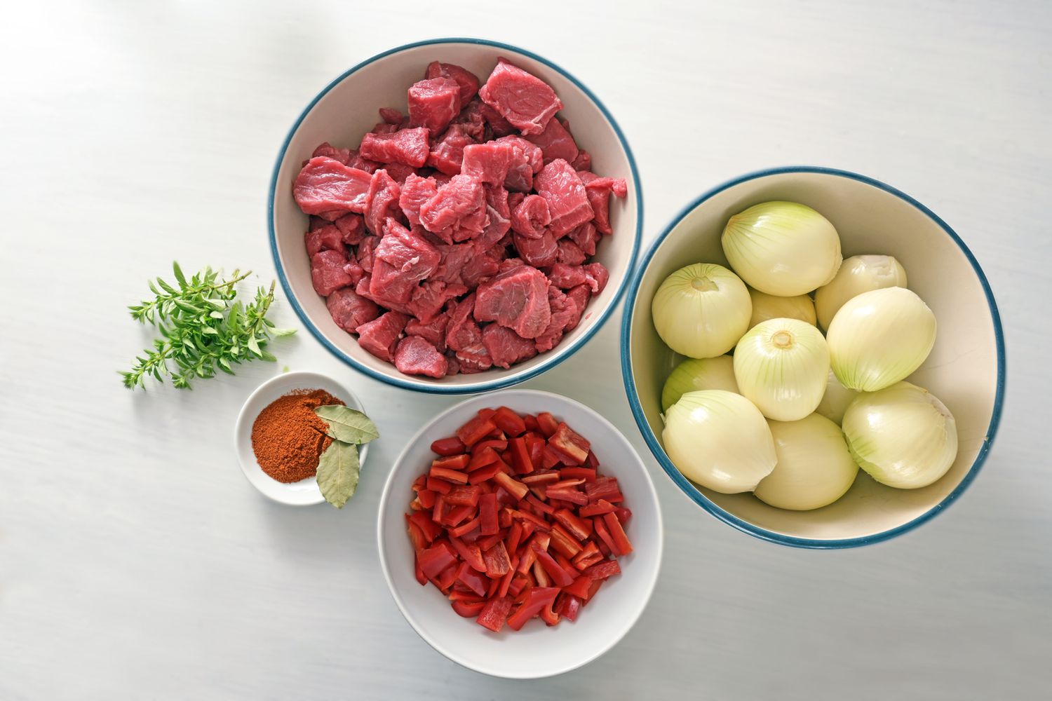 Ingredients for stew or goulash with diced beef, onions, bell pepper, herbs and spices from above on a white painted table