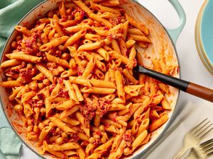 Chickpea pasta in tomato-based sauce served in a pot, with a serving spoon and nearby place settings