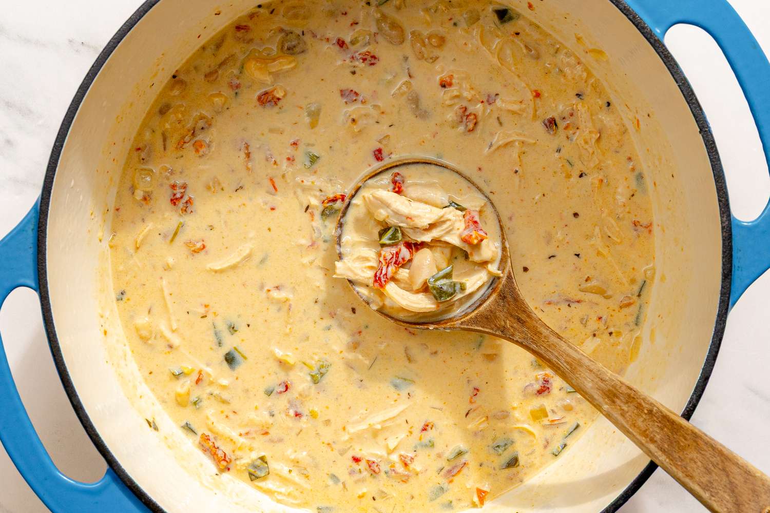 A pot of creamy Marry Me Chicken Chili with a wooden ladle containing a portion of the dish