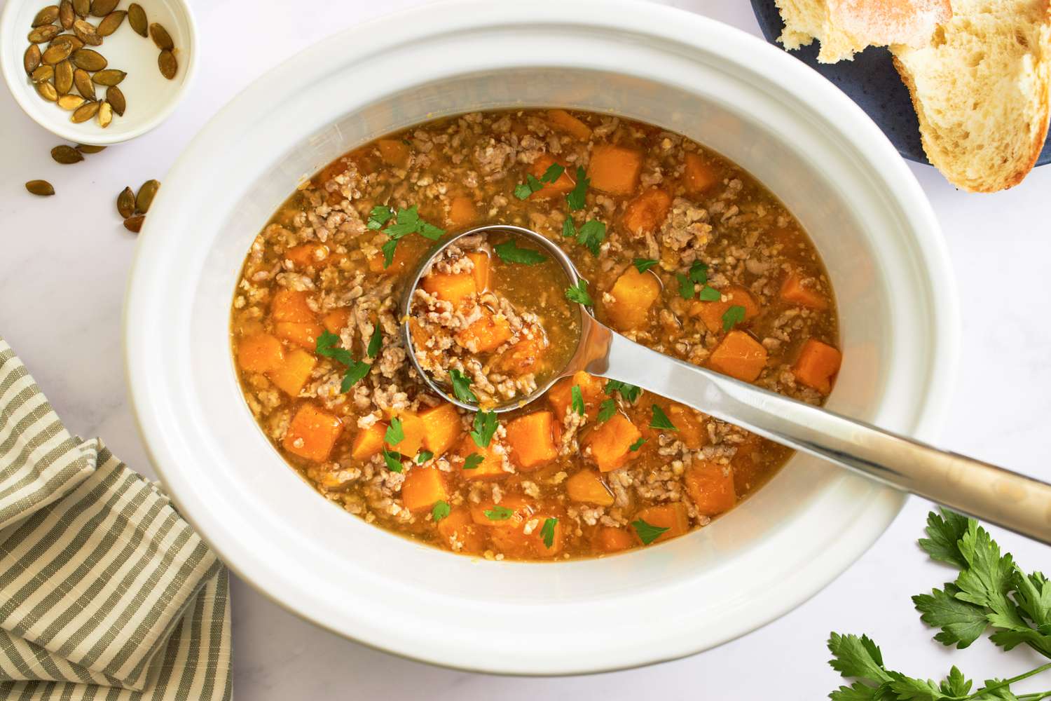 Butternut squash and sausage soup in a white bowl with a ladle